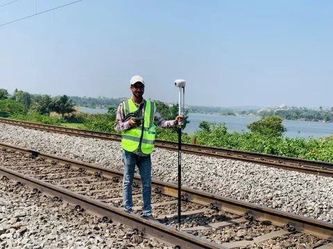 Surveyor recording levels along a railway track beside a lake